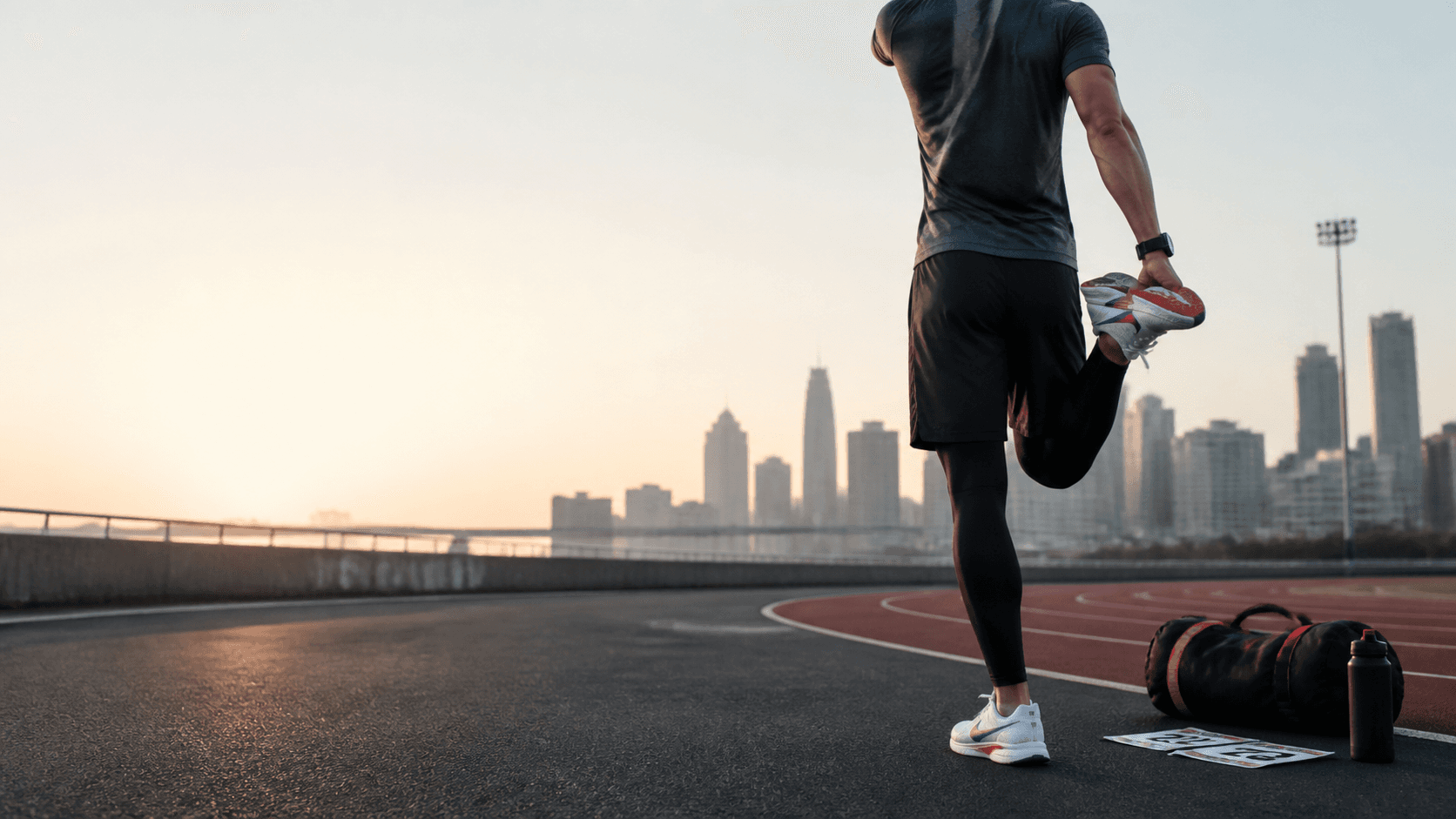 Editorial placeholder image of an athlete stretching near a track with training gear.